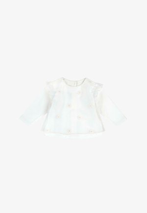 Blouse blanche à manches longues pour bébé avec superposition transparente, petites fleurs roses brodées, et détails froncés aux épaules sur fond uni.