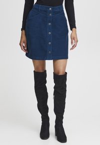 Blauwe corduroy mini-rok met een ritssluiting aan de voorkant, twee zijzakken en een gestructureerde taille. Gecombineerd met zwarte knie-hoge laarzen.