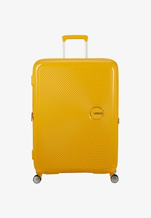 Valigia rigida gialla con texture a cerchi concentrici, manico retrattile, doppie ruote nere e argento e un accento con logo.