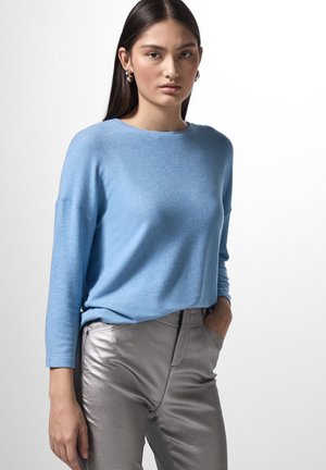 Ljusblå långärmad tröja i mjukt material, kombinerad med silverfärgade metalliska byxor med slim fit och sidfickor.