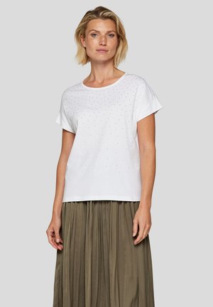 Weißes Baumwoll-T-Shirt mit runder Ausschnitt, kurzen Ärmeln und verstreuten dekorativen Nieten auf der Vorderseite, kombiniert mit einem plissierten olivgrünen Rock.