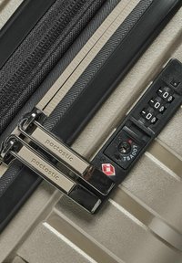 Primo piano delle zip di una valigia silver con il marchio "pactastic" accanto a un lucchetto combinato approvato dalla TSA impostato su 0-0-0.