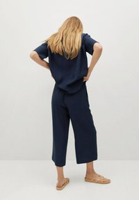 Námořnický modrý, volný top s krátkými rukávy, doplněný širokými kalhotami. Hladká tkanina, jednoduchý design a ploché sandály dotvářejí vzhled.