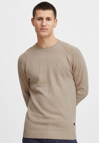 Beige strikket sweater med rund halsudskæring, ribbede manchetter og kant. Har et lille logo på brystet og en struktureret overflade.