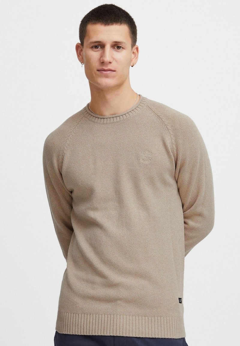 Beige strikket sweater med rund halsudskæring, ribbede manchetter og kant. Har et lille logo på brystet og en struktureret overflade.