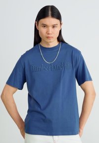 Σκούρο μπλε βαμβακερό μπλουζάκι με στρογγυλή λαιμόκοψη και κοντά μανίκια, που διαθέτει ανυψωμένο λογότυπο Timberland και απαλό υφή.