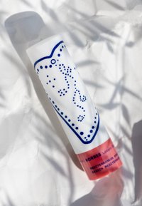 Tubo blanco con diseño y borde de puntos azules; sección inferior rosa etiquetada como "KORRES Lip Balm." Textura suave, forma cilíndrica.