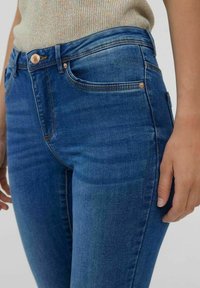 Jeans de mezclilla azul con un corte ajustado, que presentan un desvanecimiento sutil, herrajes de cobre, cinco bolsillos y un diseño de cintura de altura media.