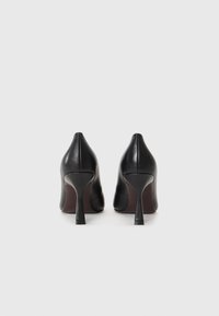 Chaussures à talons aiguilles noires en cuir avec un bout pointu et un talon stiletto étroit. Texture lisse, design minimaliste et sans motifs visibles.