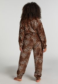 Brūnu un krēmkrāsas leopardu raksta mājas apģērba komplekts, kas izgatavots no mīkstas, greznas auduma; iekļauj brīva piegriezuma topu un bikses ar manšetēm ap potītēm.