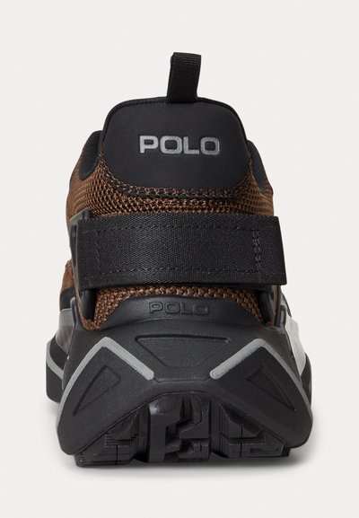 Smešane smeđe tenisice s crnim naglascima, koje imaju istaknut remen i teksturiranu gumenu petu. "POLO" logo je prikazan na peti.