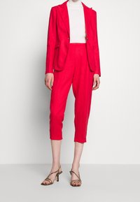 Bright pink linen suit with a tailored blazer and cropped trousers. Worn with a fitted white turtleneck and strappy beige high heels.