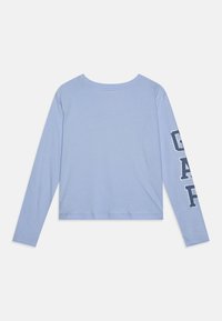 Ljusblå långärmad skjorta med rundad halsringning, med en grafisk logga tryckt i mörkblått på vänster ärm. Mjuk tygtextur.