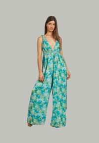 Kombinezon w kwiatowy wzór w odcieniach niebieskiego i zielonego, z głębokim dekoltem w kształcie litery V, szerokimi nogawkami i związanymi ramiączkami. Lekki materiał.
