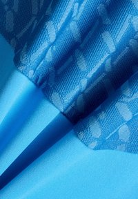 Blauwe stof in close-up die het textuurcontrast toont tussen gladde en patroongebreide delen met geometrische ontwerpen.