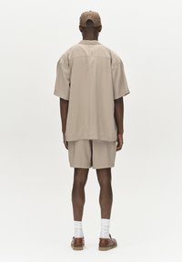 Camicia beige a maniche corte e pantaloni corti abbinati in tessuto leggero. Indossati con calze bianche e scarpe marroni. Il cappellino si abbina al colore dell'outfit.