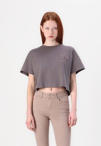 Gray cropped t-shirt with a round neckline and short sleeves, featuring a logo in red and black. Paired with light beige slim-fit jeans.