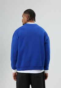 Blauwe trui met een ontspannen pasvorm, ronde hals en contrasterende witte manchetten. Gemaakt van getextureerde katoenen stof, voorzien van verlaagde schouders.