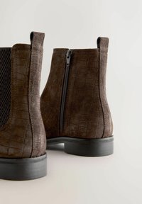 Pruunist sametist pahkluu saapad on krokodillimustriga, külgsi tõmblukuga ja musta kummi tallaga. Kujundus on klassikaline ja madala kontsaga.