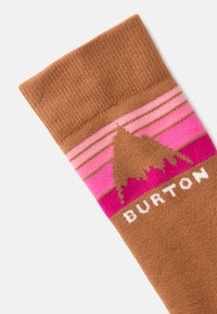 Brūns adīts zābaciņš ar rozā un baltām svītrām, ar kalna grafiku un "BURTON" tekstu baltā krāsā apakšā. Mīksta tekstūra.