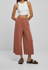Lehké kalhoty culotte v barvě terakoty s elastickým pasem, v kombinaci s bílým tílkem bez rukávů a černými nízkými sandály.