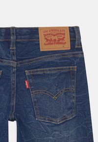 Mörkblå denimjeans med en brun läderlapp som har "Levi Strauss & Co."-logotypen, synliga sömmar och en liten röd tagg på sidan.