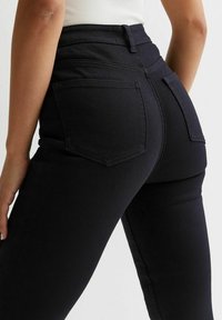 Svarta högmidjade jeans med en figursydd design, som har två bakfickor och ton-i-ton sömnad. Slät denimtextur med en lätt elastisk känsla.