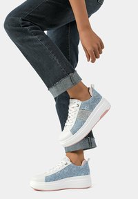 Sneakers platform azzurro chiaro con dettagli bianchi, in materiale denim, decorati con glitter e suola bianca chunky, abbinati a jeans scuri.