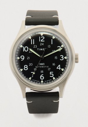 Analog wristwatch with black dial, white numerals (12-hour and 24-hour), luminous hands, stainless steel case, and black leather strap.