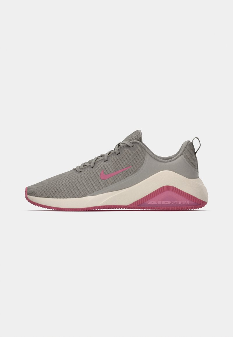 Nike Air Zoom shoes in grey mesh with pink accents. Features a rounded toe, lace-up design, and a textured rubber sole with pronounced tread.