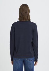 Pull à manches longues bleu marine en tissu lisse, avec un col rond et une coupe droite. Porté avec un jean denim bleu.