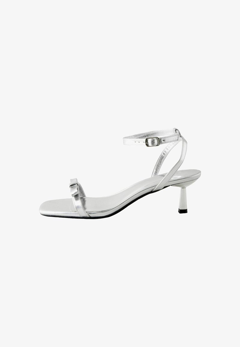Hõbedane kontsaga sandaal ruuduotsaga, õhuke pahkluu rihm ja väike plokkkonts. Sile metallpind ja minimalistlik disain.