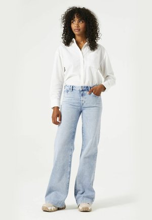 Jean taille haute bleu clair avec une coupe décontractée, associé à une chemise blanche à boutons. La tenue présente un minimum de détails et une texture lisse.