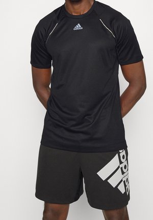 Homme portant un t-shirt de sport noir à manches courtes Adidas et un short noir Adidas avec un grand logo blanc sur la jambe gauche.