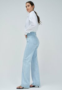 Jeans de tiro alto en azul claro con pierna recta, confeccionados en denim. Presentan un diseño clásico de cinco bolsillos y detalles de costura mínimos.