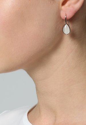 Boucles d'oreilles goutte avec un centre ovale blanc lisse et un crochet en métal argenté fin. Design simple et minimaliste.