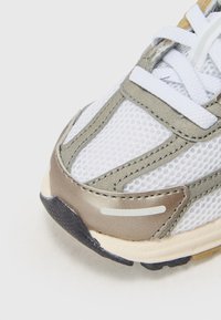 Weißer Sportschuh mit Mesh-Gewebe, silbernen Akzenten und einer abgerundeten Zehenpartie. Verfügt über eine strukturierte Gummisohle und flache weiße Schnürsenkel.
