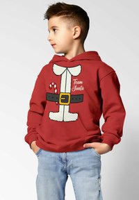 Red hooded sweatshirt featuring playful Santa-themed graphic, including a belt, fur accents, and a candy cane. Casual fit with front pocket.