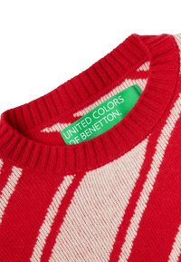 Červeno-bílý pruhovaný svetr s žebrovaným límcem. Viditelná zelená etiketa s nápisem "UNITED COLORS OF BENETTON". Jemná pletená textura.