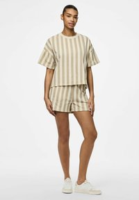 T-shirt corta a righe beige e pantaloni corti coordinati in tessuto morbido. Indossati con sneakers bianche, con accenti sottili e una vestibilità comoda.
