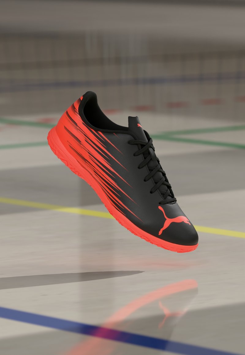 Zapatilla deportiva negra con acentos rojos, que presenta una superficie lisa, diseño elegante y franjas contrastantes. Cierre de cordones y suela de goma.