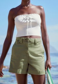 Valkoinen olkaimeton ribbineulottu crop top, jossa etuosassa solmimisyksityiskohta, yhdistetty oliivinvihreisiin korkeavyötäröisiin shortseihin, joissa on napit ja sivutaskut.