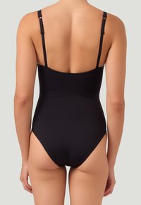 Kvinna i en svart baddräkt med tunna justerbara axelband, visad bakifrån mot en enhetlig bakgrund.