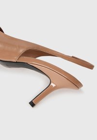 Chaussures à talons hauts en cuir verni nude avec bout ouvert, conception slingback et talon fin. Texture lisse avec une finition brillante.