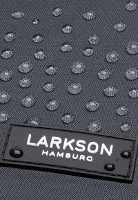 Fekete szövet táska kiemelkedő vízcseppekkel, texturált felülettel és egy téglalap alakú fekete címkével, fehér, dombornyomott szöveggel: "LARKSON HAMBURG."