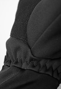 Schwarzer textile Handschuh mit einem genähten, elastischen Bündchen und einer glatten, nahtlosen Textur. Klettverschluss im oberen Bereich sichtbar.