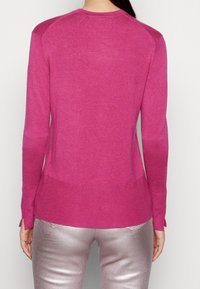Vysoce přiléhavý svetr s dlouhým rukávem v jasně růžové pletenině, s žebrovaným lemem a manžetami, a ramenními akcenty s mírně odlišnou texturou.