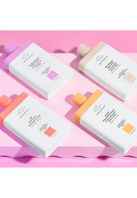 Vier elegante, beschriftete Flaschen mit Körperpflegeprodukten in sanften Farben sind vor einem weichen rosa Hintergrund ordentlich angeordnet.