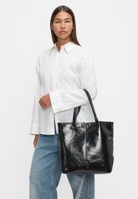 Czarna skórzana torba na ramię o gładkiej fakturze i błyszczącym wykończeniu, z podwójnymi uchwytami i bez widocznych elementów metalowych.