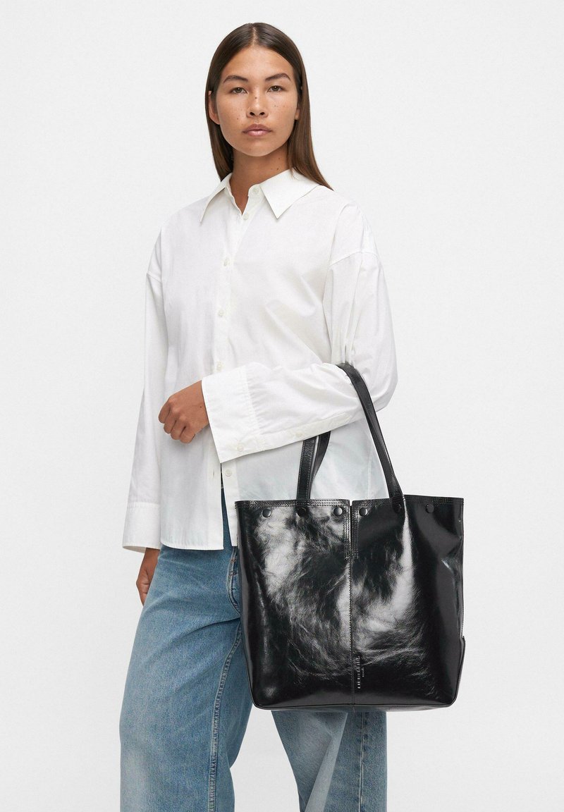 Czarna skórzana torba na ramię o gładkiej fakturze i błyszczącym wykończeniu, z podwójnymi uchwytami i bez widocznych elementów metalowych.